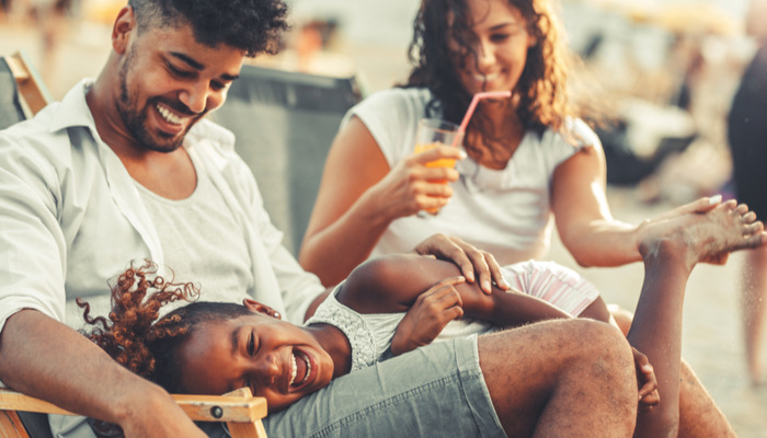 Young mixed race family laughing sitting and relaxing at the beach on beautiful summer day on their vacation